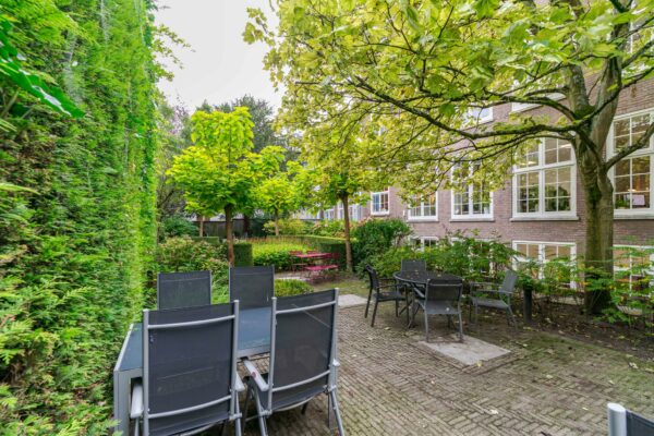 Binnentuin met terrasmeubilair, omgeven door groen en een woongebouw aan het Lange Voorhout.
